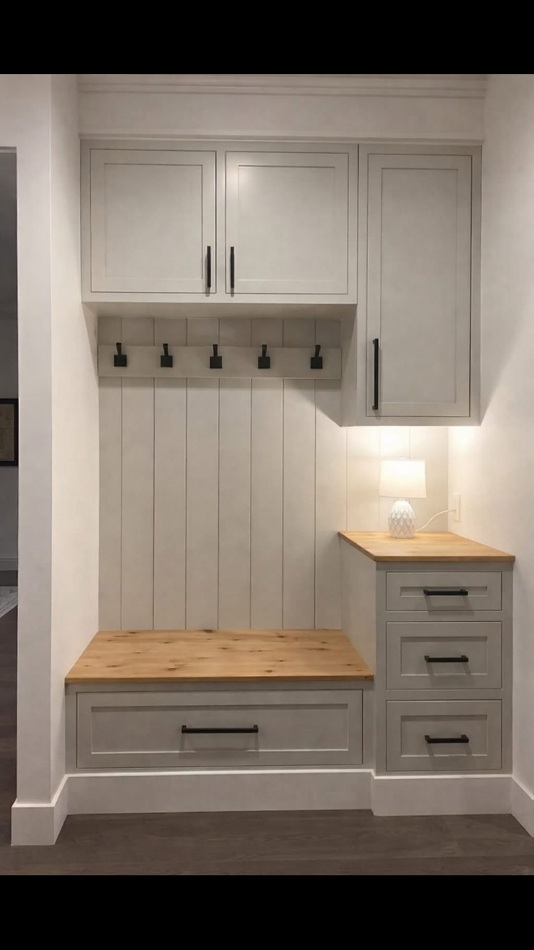 Built-in entryway storage: gray cabinets, wooden bench, hooks, drawers, and small lamp with warm light.