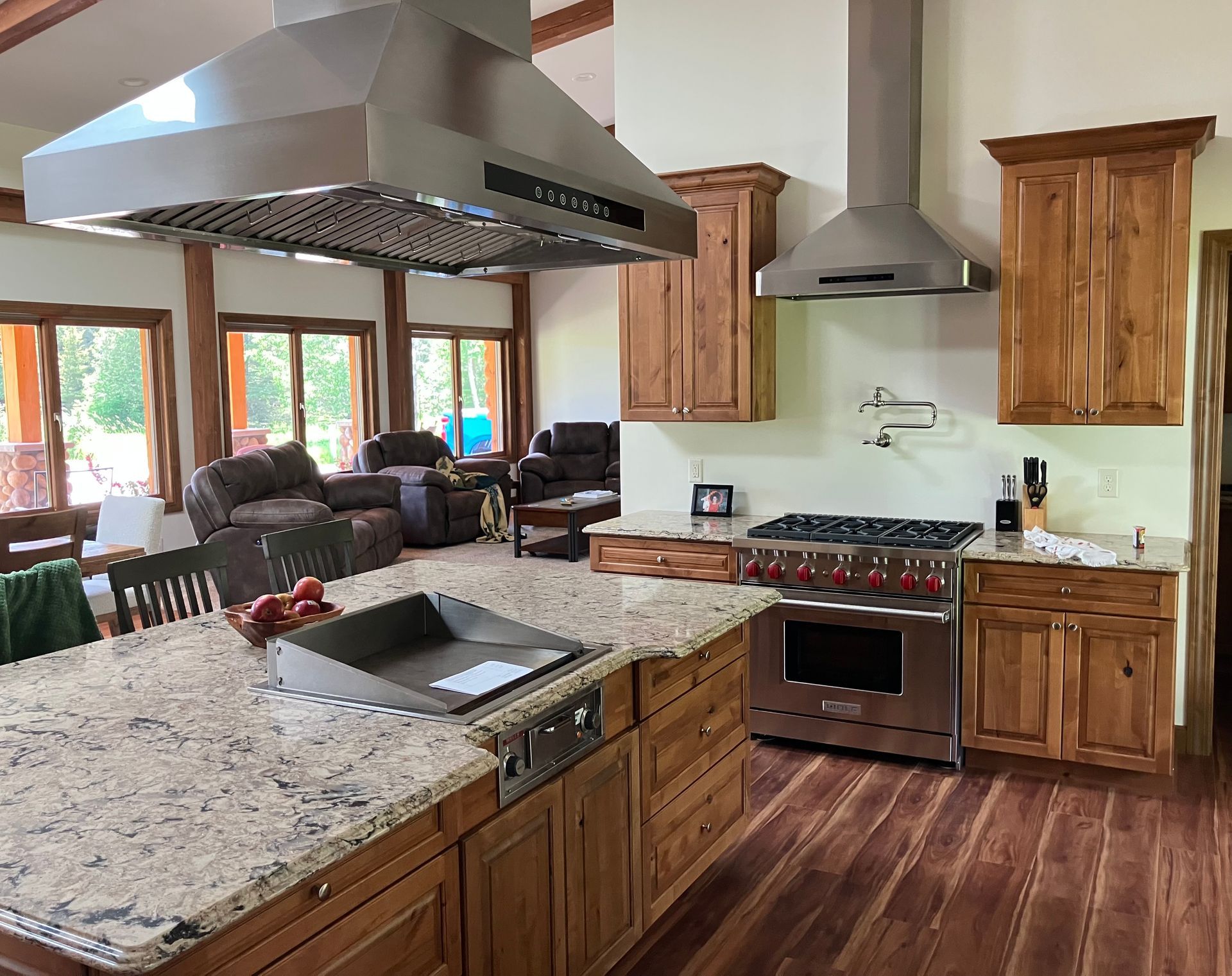 Kitchen with island, range, cabinets, and stainless steel range hoods. Wooden floors and natural light.