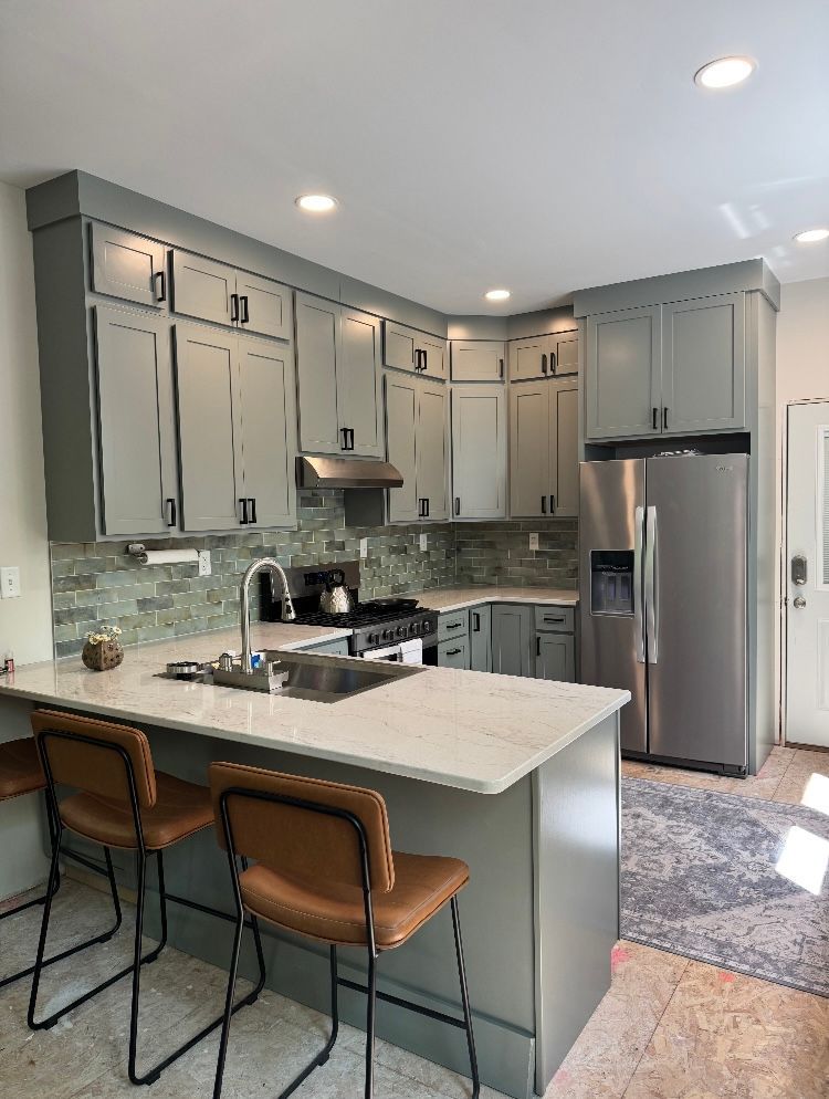 Modern gray kitchen with stainless steel appliances, white countertop, brown bar stools.