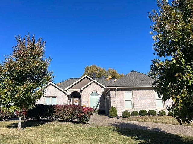 A brick house with a gray roof and trees in front of it