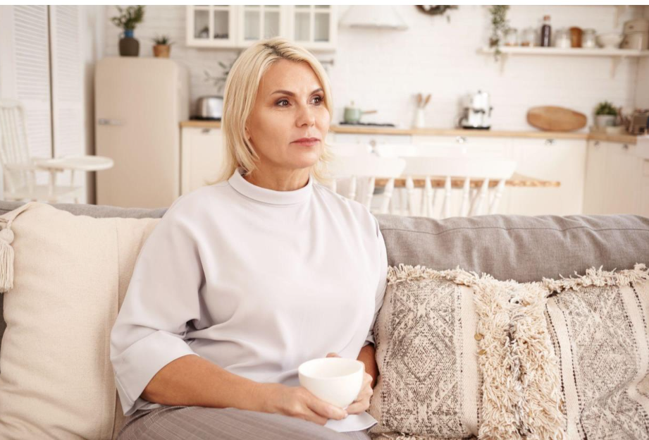 Woman sitting on a couch holding a cup in a bright living room