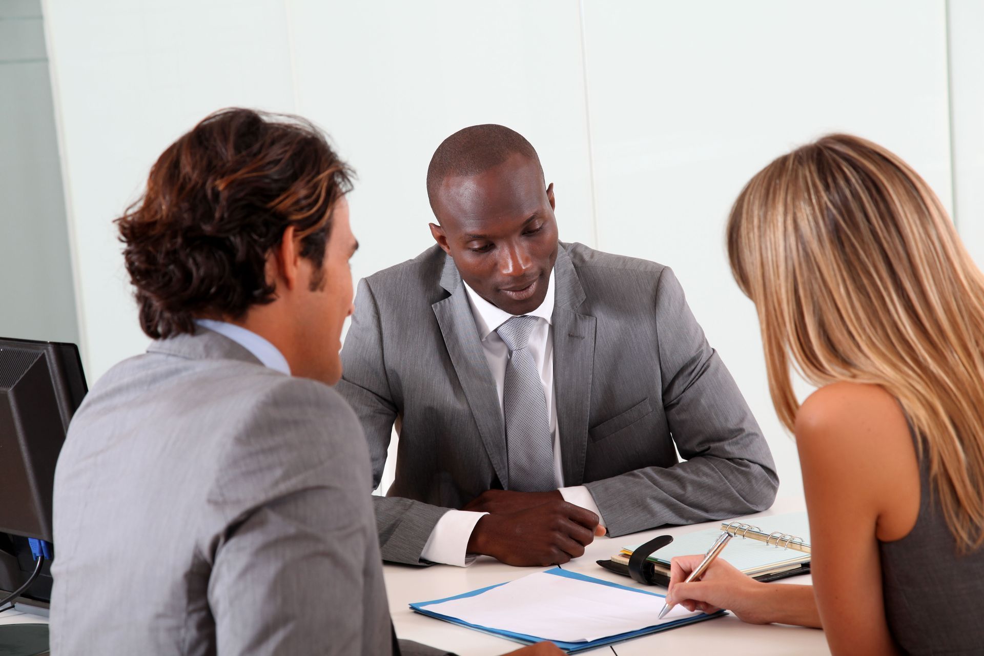 Three people in a business meeting reviewing documents at a table