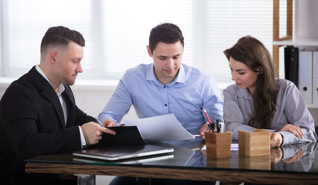 Three people reviewing documents at a conference table in a bright office