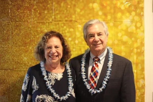 Two smiling people in formal attire standing before a gold, textured backdrop