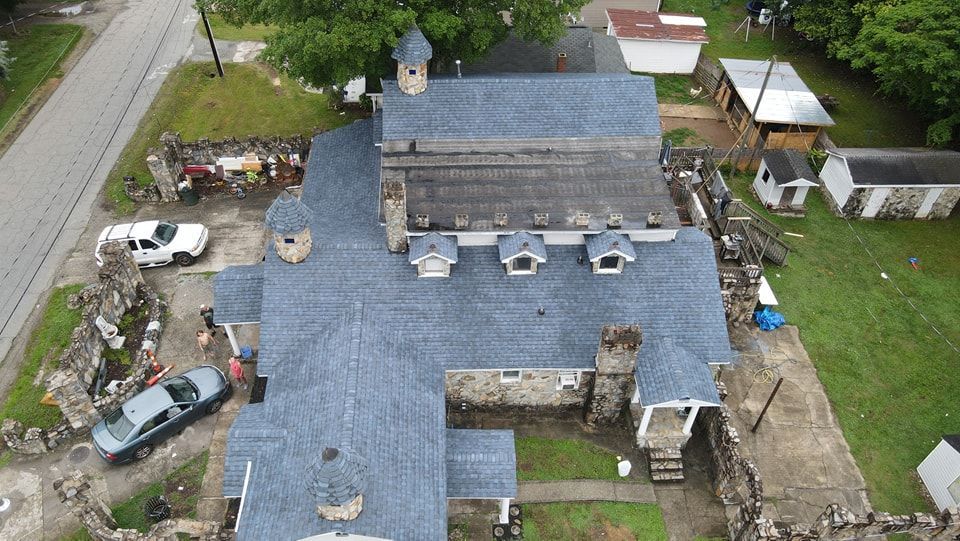 Aerial view of a stone building with blue roofs, turrets, and a lawn. Cars and a shed are nearby.