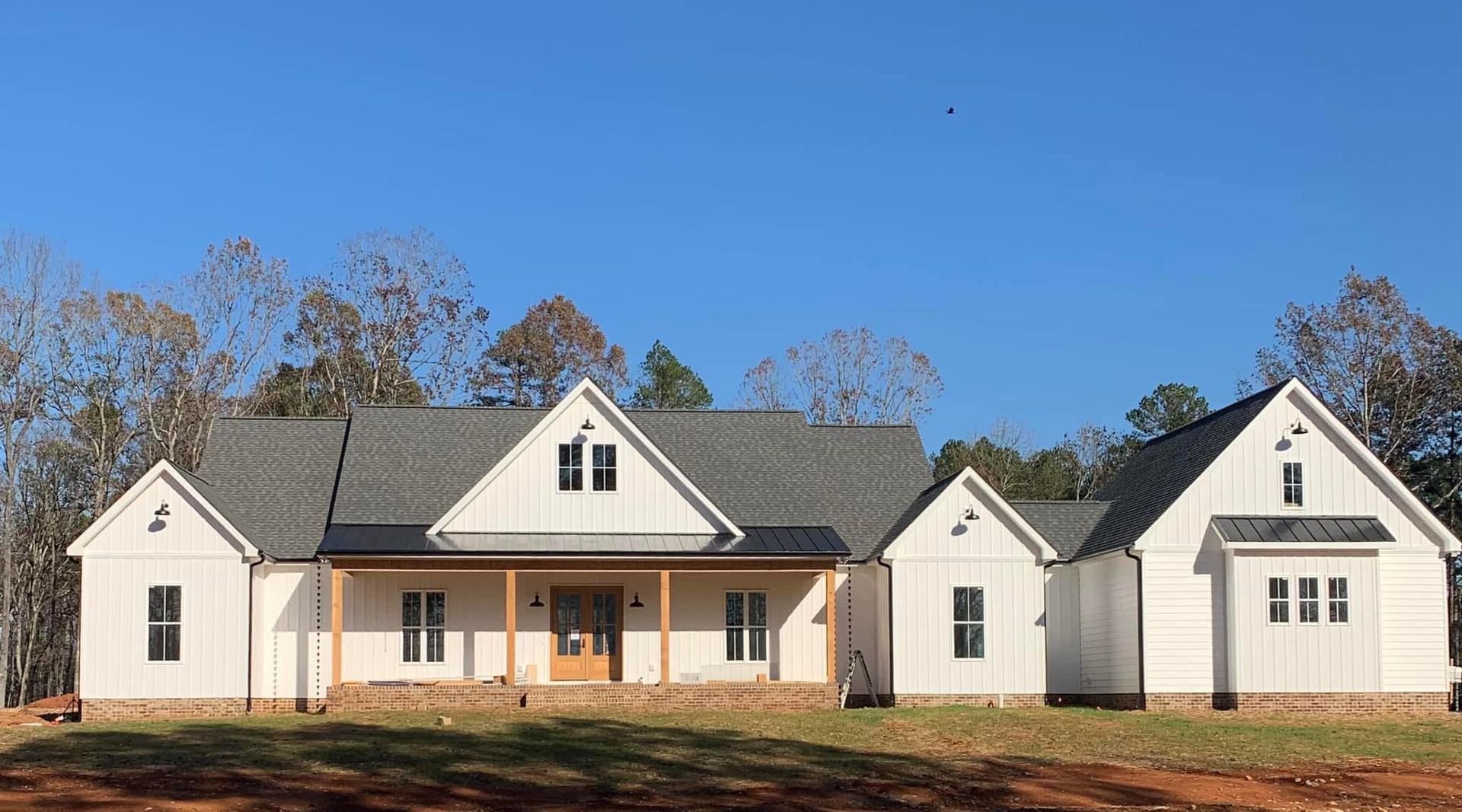 White farmhouse under construction with multiple gables and a porch, set against a clear blue sky.