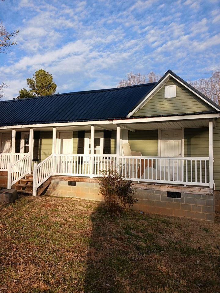 Green house with white porch and railings under a blue and cloudy sky.