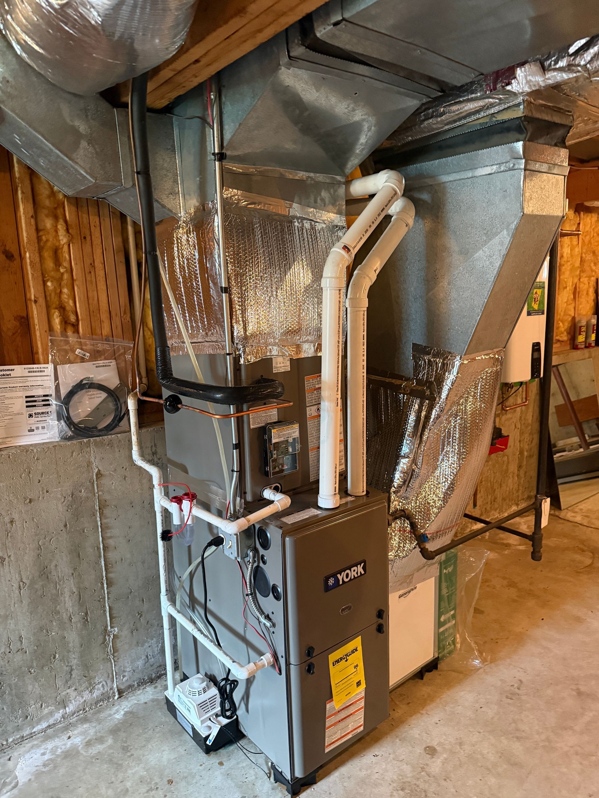 Furnace and ductwork in a basement utility room with exposed insulation and pipes