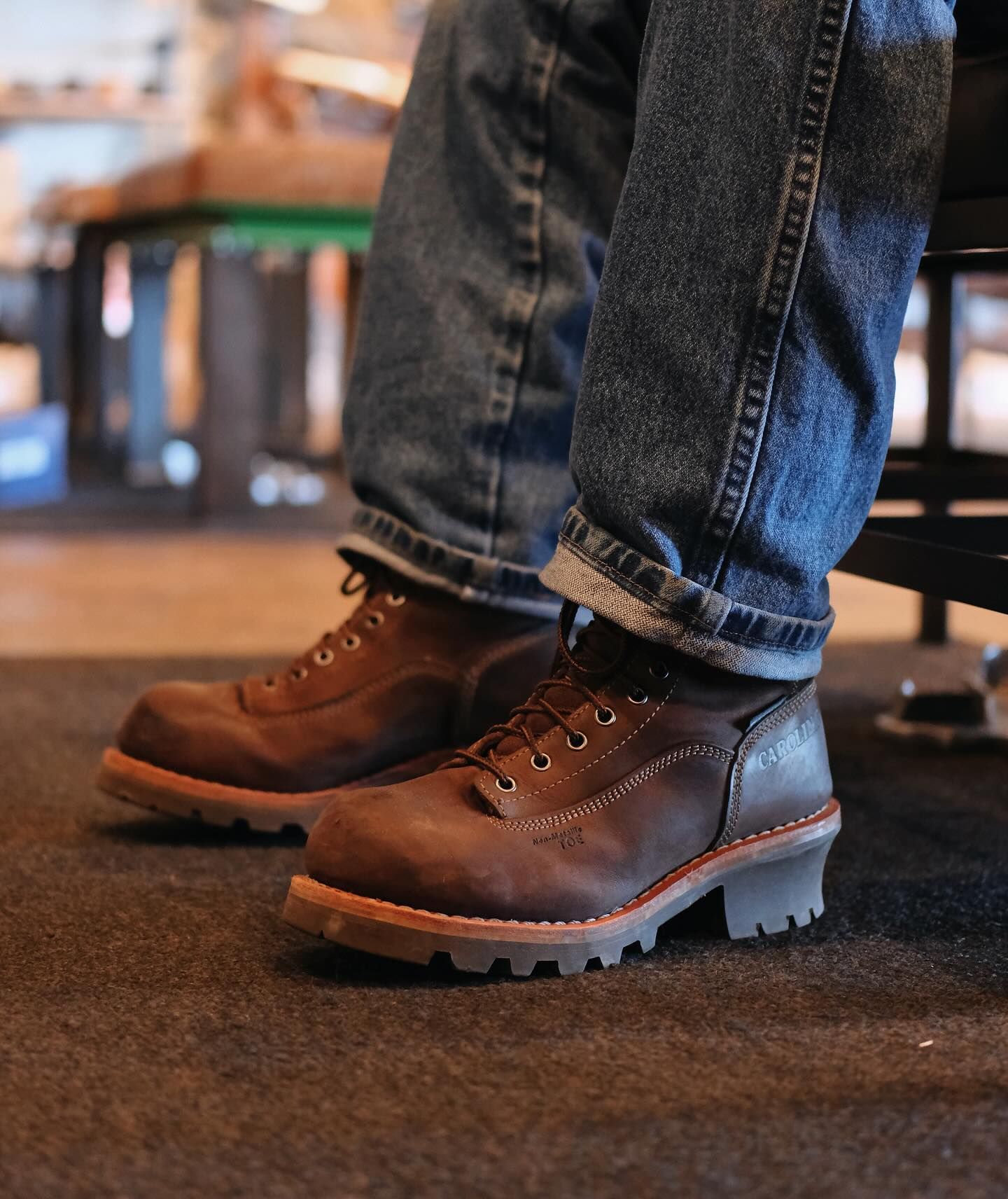 Person wearing brown work boots and blue jeans, cuffed at the ankles.