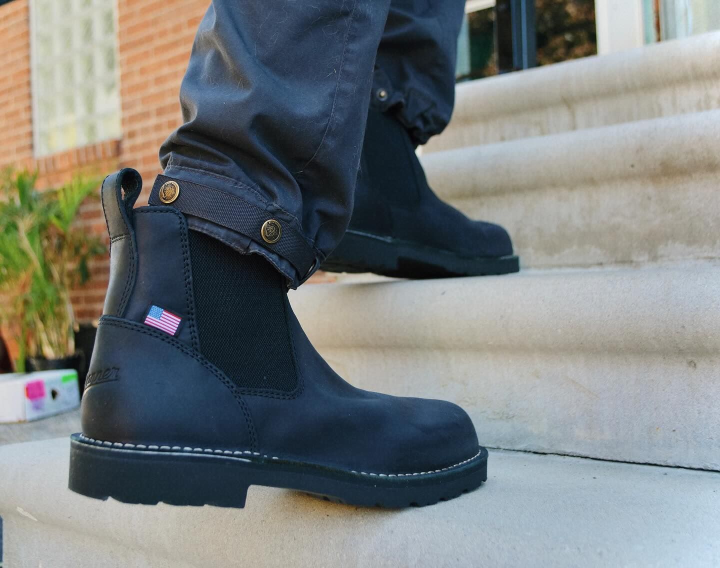 Black work boots on a person stepping up outdoor stairs, with dark pants and a building background.