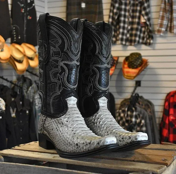 Cowboy boots, black uppers, light gray snakeskin vamps, sitting on a wooden surface in a store.