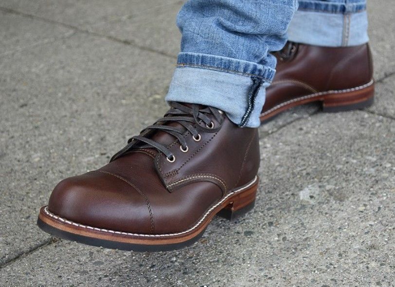 Person wearing brown leather boots with light blue jeans, standing on a concrete surface.