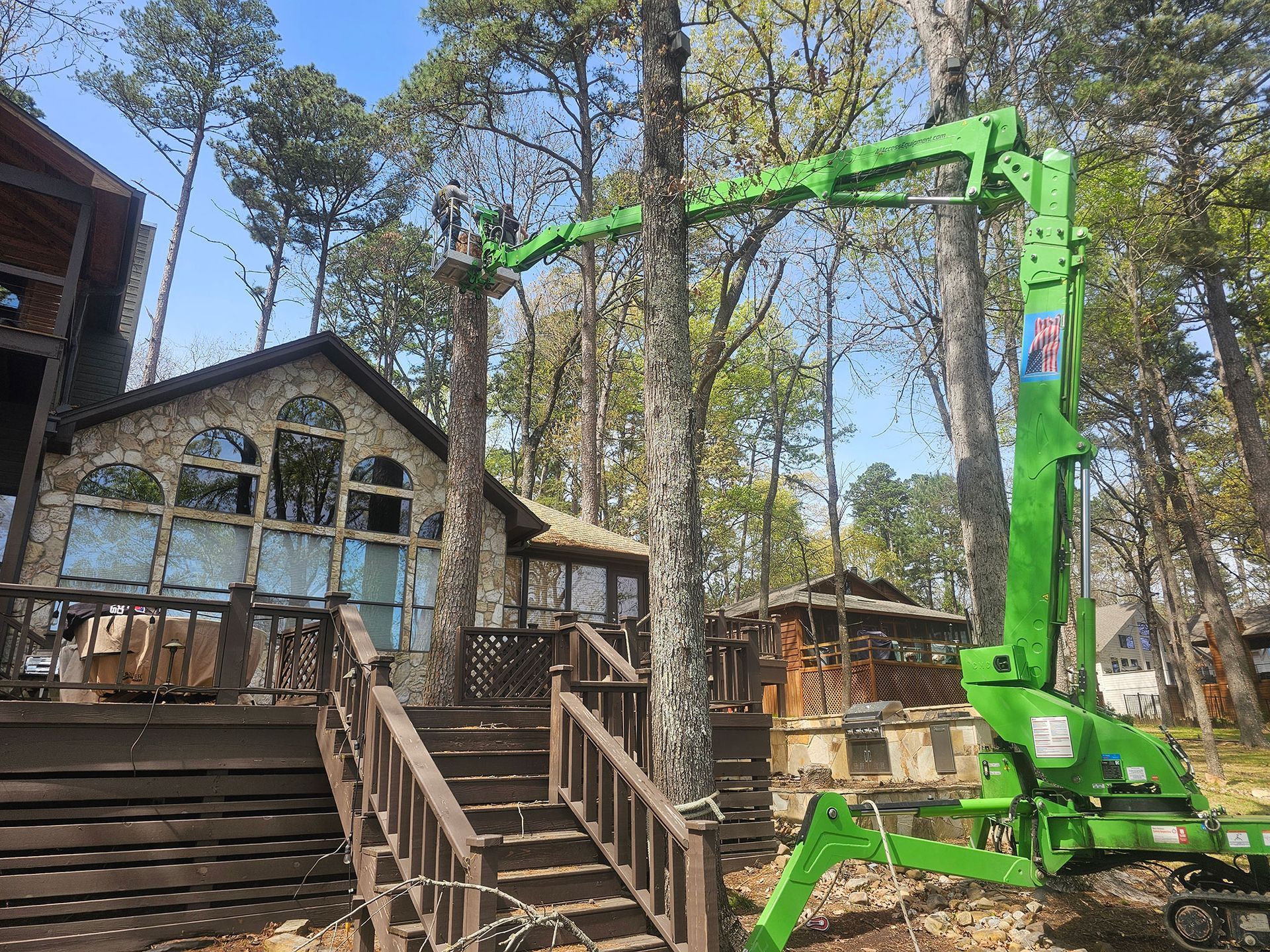 Green construction crane beside a wooden house and deck in a wooded yard