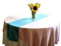 A table with a table runner and a vase of sunflowers on it.