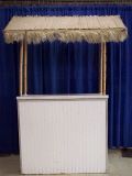 A white table with a thatched roof is sitting in front of a blue curtain.