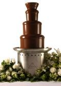 A chocolate fountain is surrounded by flowers on a table.