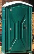A green portable toilet is sitting in front of a brick building.