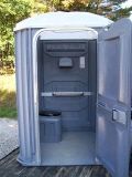 A portable toilet with the door open is sitting on a wooden deck.