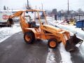 A yellow backhoe is parked on the side of a snow covered road.