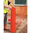 A man is standing next to a roll of orange fence.
