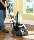 A man is using a machine to sand a hardwood floor.