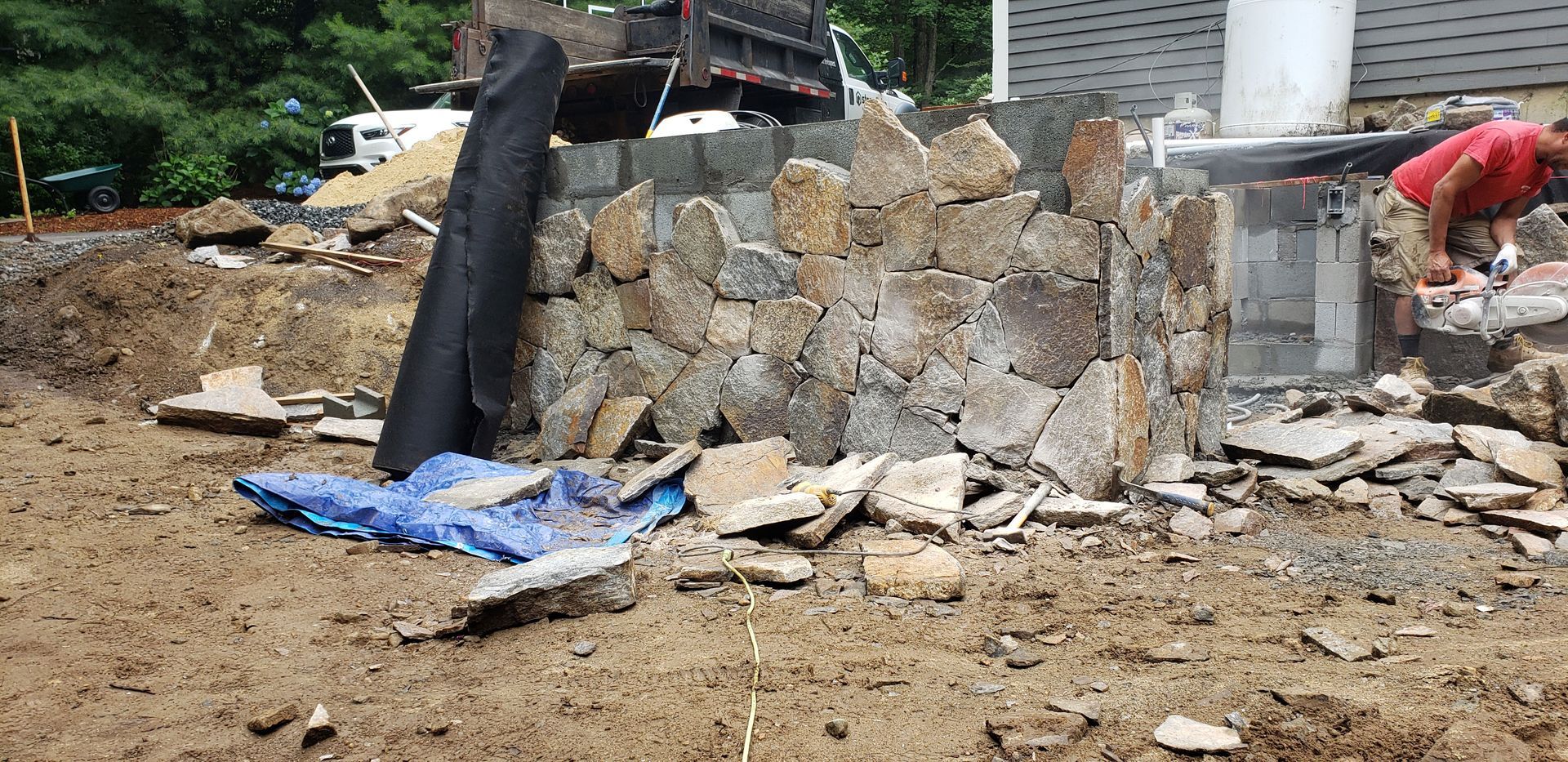 Collapsed stone wall at a construction site with rubble, a blue tarp, and workers nearby