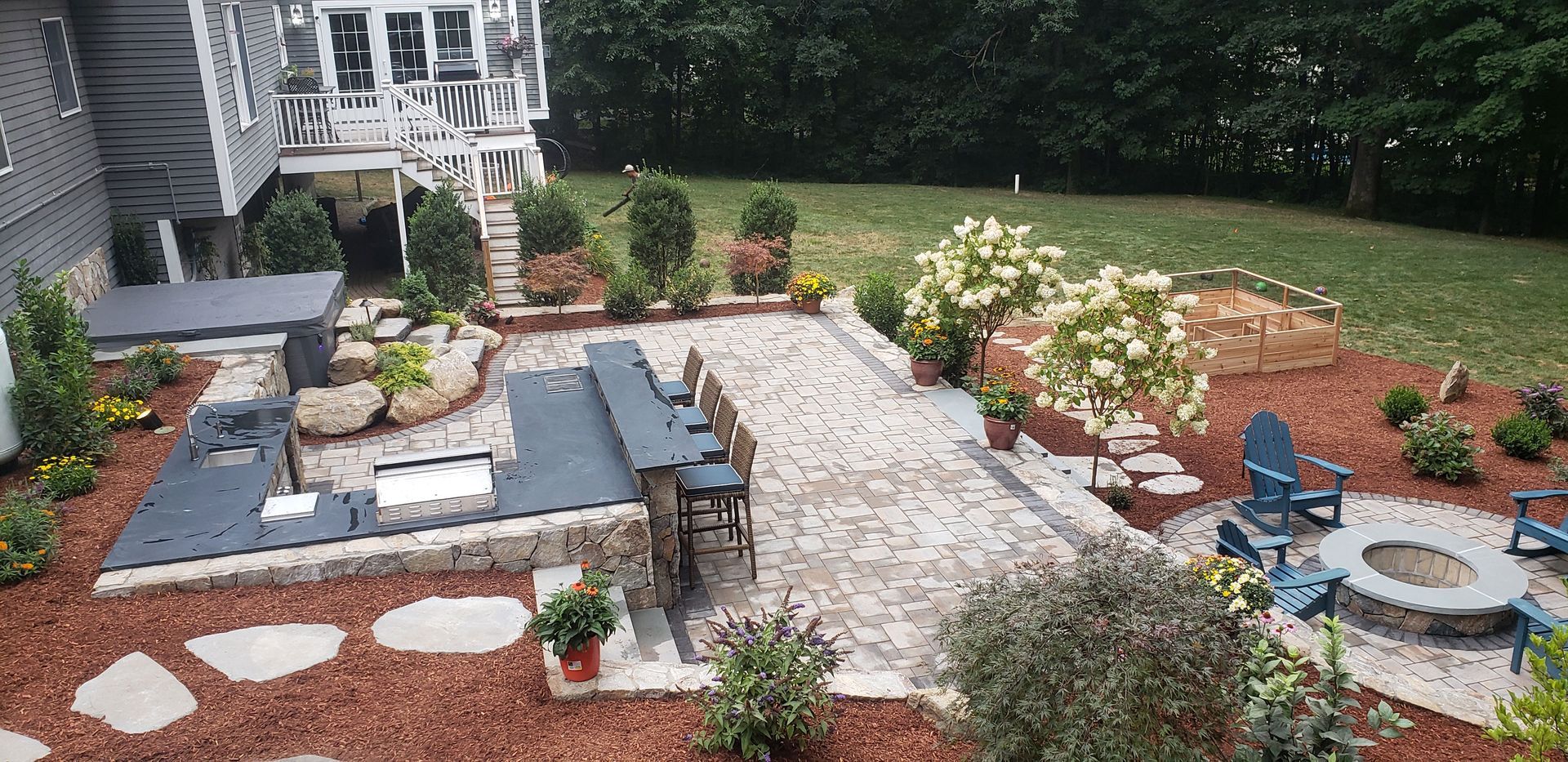 Landscaped backyard patio with stone pavers, seating, flower beds, and a small pond fountain