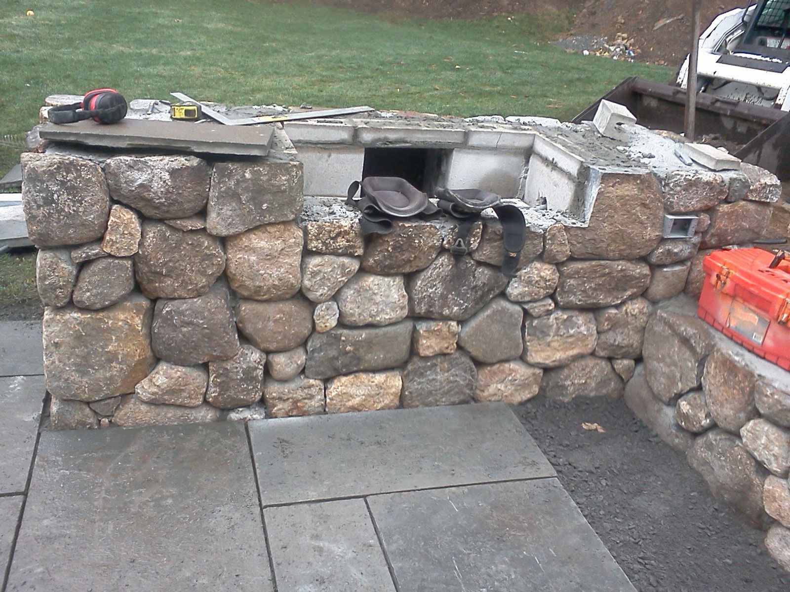 Stone outdoor wall with a flat cap, built-in fire pit opening, and paving stones in front