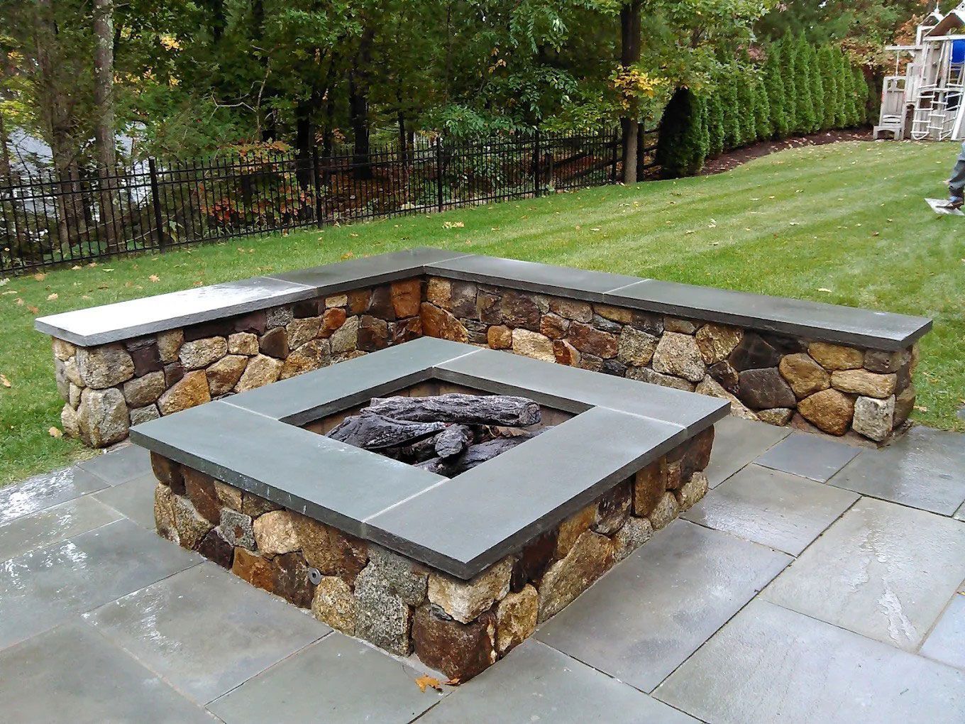 Stone fire pit with gray cap in a landscaped backyard patio area