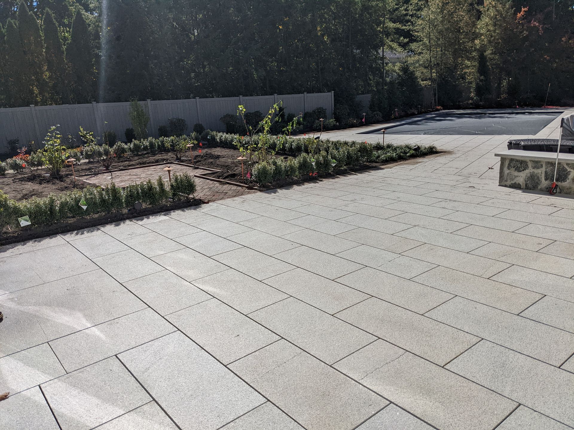 Empty paved plaza beside flower beds and trees in bright sunlight