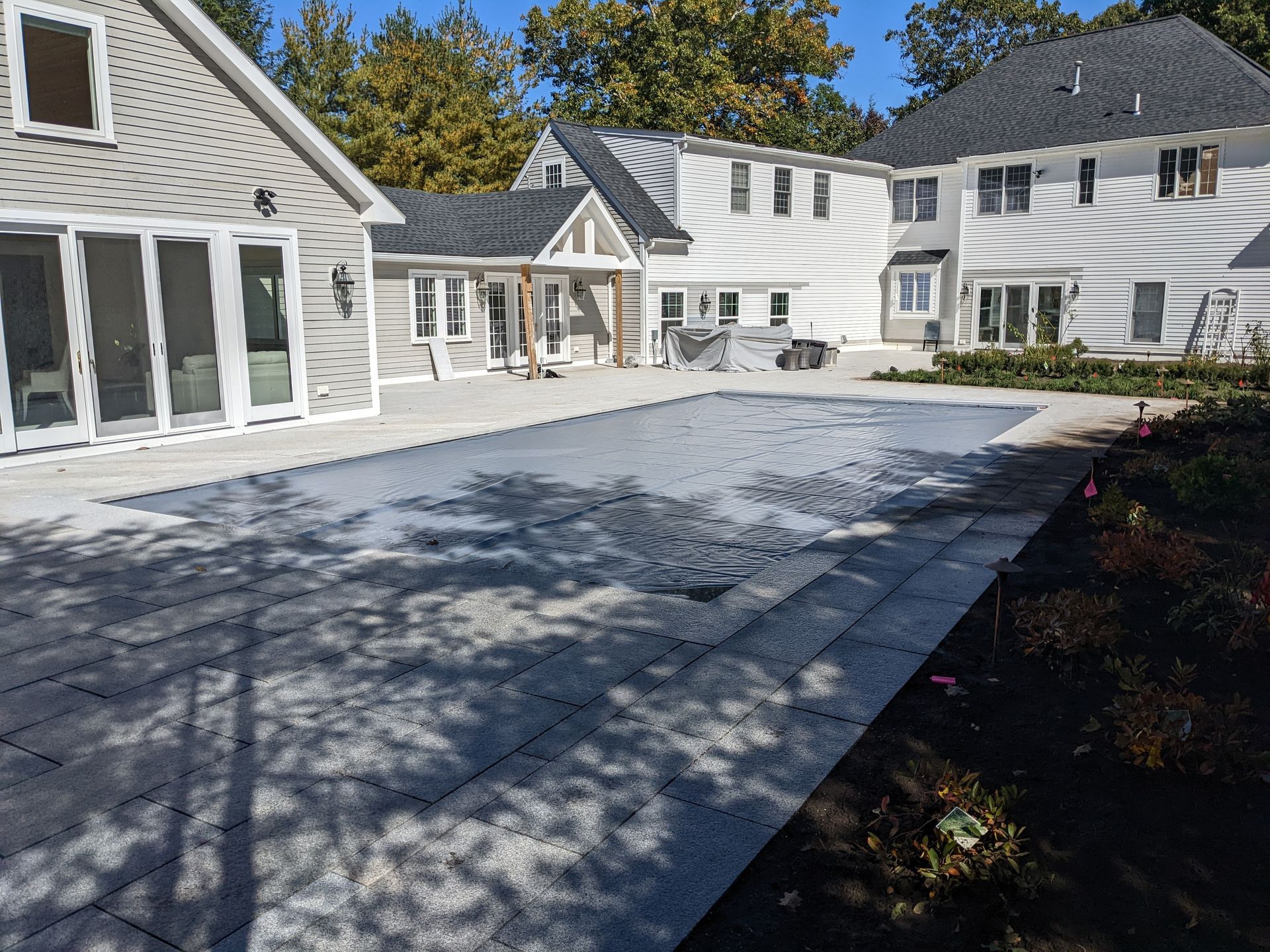 Residential backyard patio with gray pavers, white houses, and autumn shadows under a blue sky
