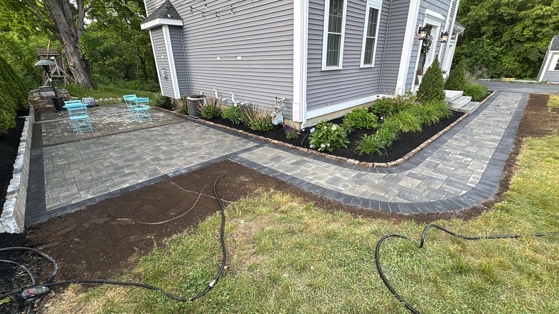 Newly paved dark gray walkway curving around a house with fresh landscaping