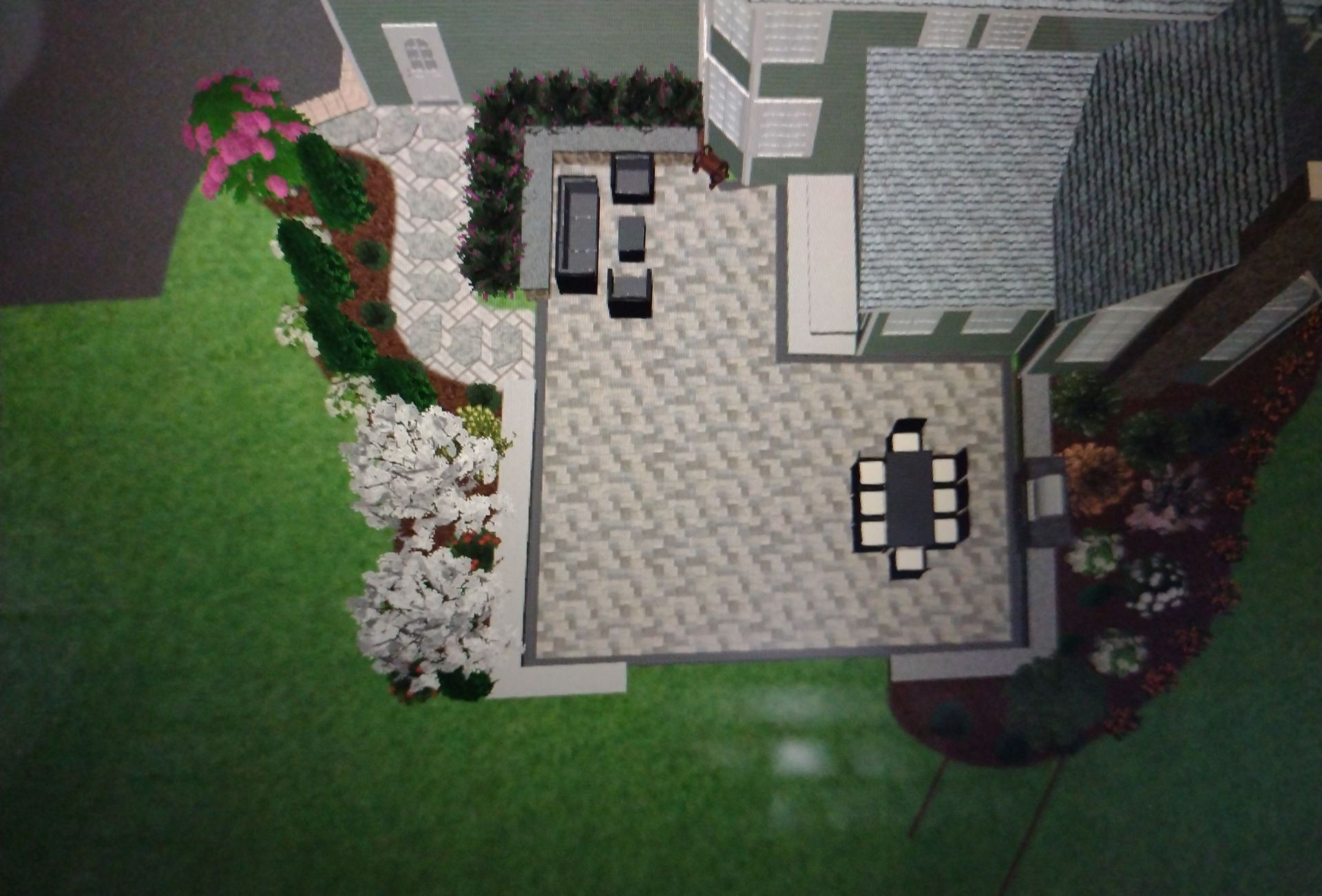 Top-down view of a modern patio with stone flooring, outdoor table, chairs, grill, and landscaped garden border