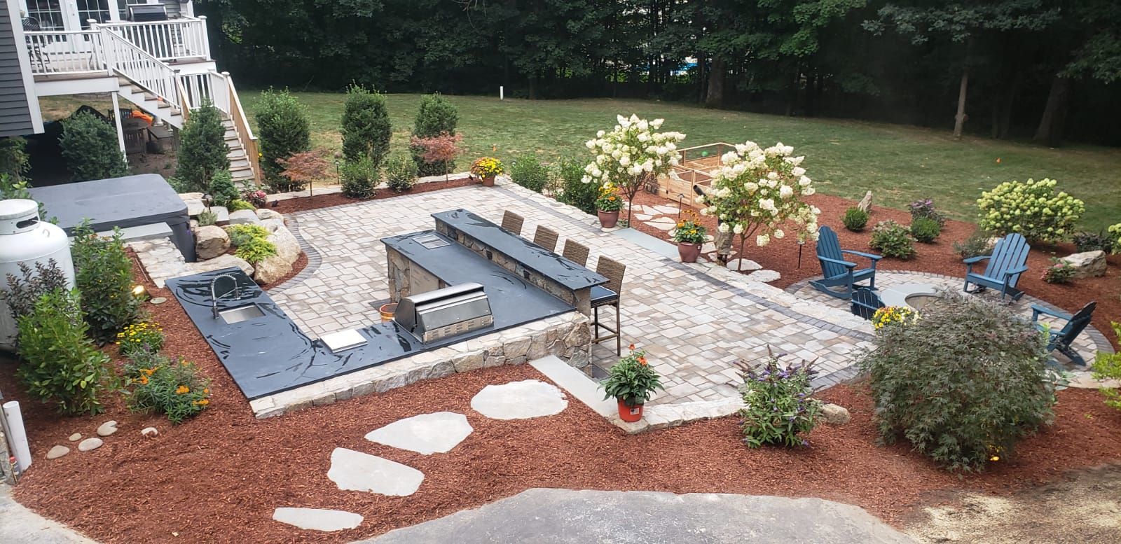 Backyard patio garden with stone steps, benches, potted plants, and a gravel path