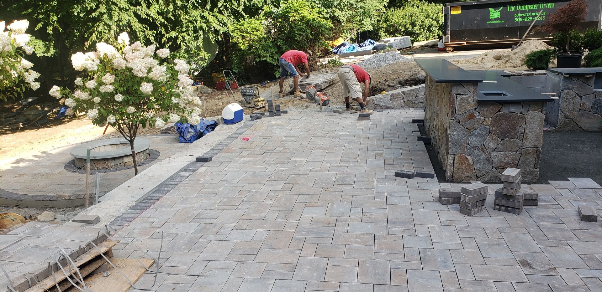 Stone walkway under construction with workers, tools, and materials along a landscaped path