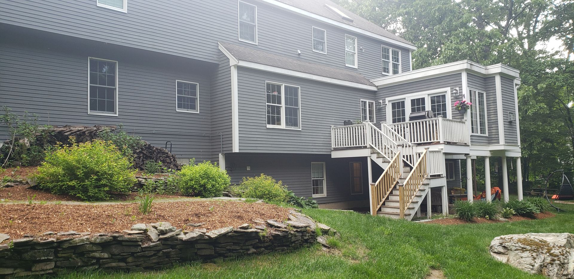 Gray house with white porch and stairs, surrounded by trees and a landscaped yard