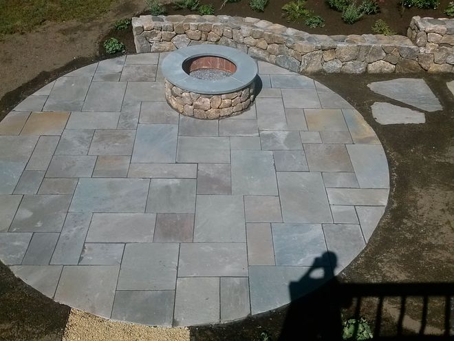 Circular stone patio with a fire pit and surrounding walkway in a backyard