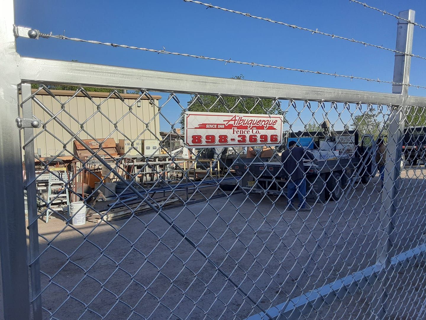 Chain link fence with a gate, a sign with a phone number, and a glimpse of equipment behind it.