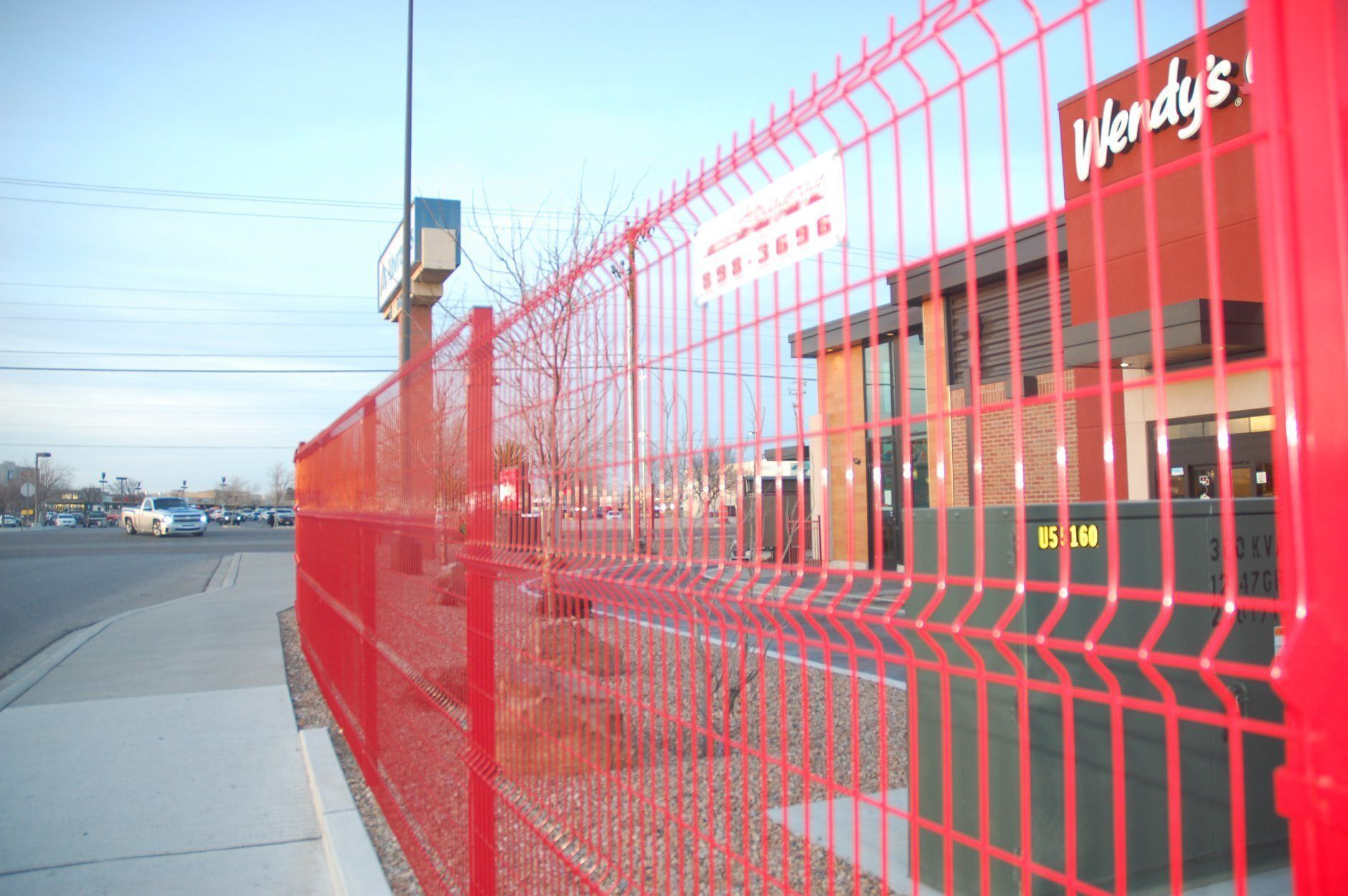 Red security fence in front of a Wendy's restaurant on a city street.