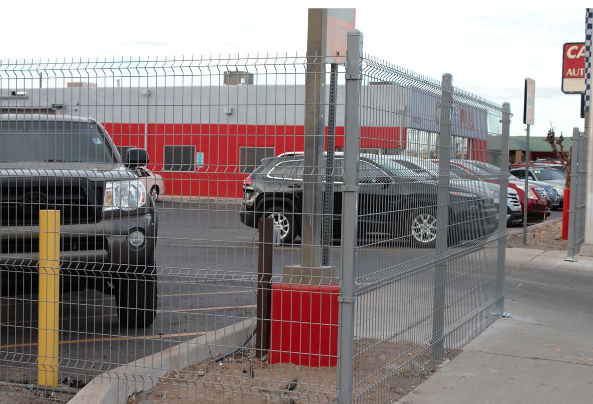 Cars parked behind a chain link fence in front of a building with red and white siding.