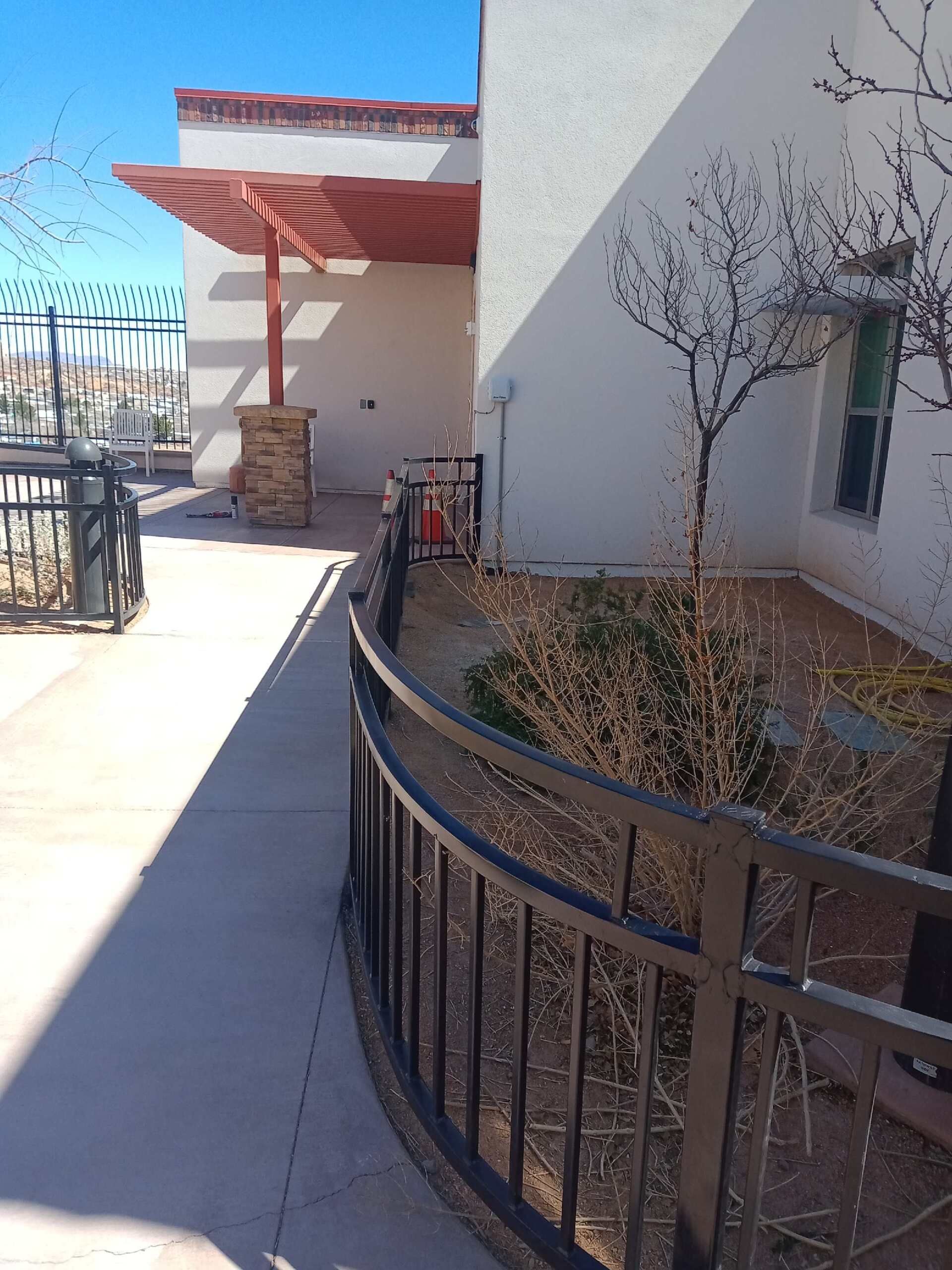 Exterior view of a building with a walkway, black metal fence, and pergola with red roof.