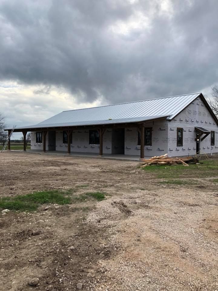 A large white house with a metal roof is being built in a dirt field.