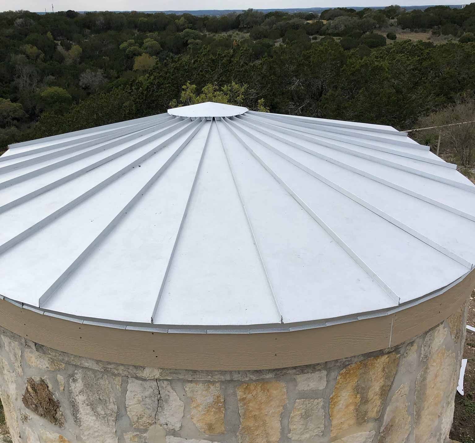 A round metal roof on top of a stone building with trees in the background.