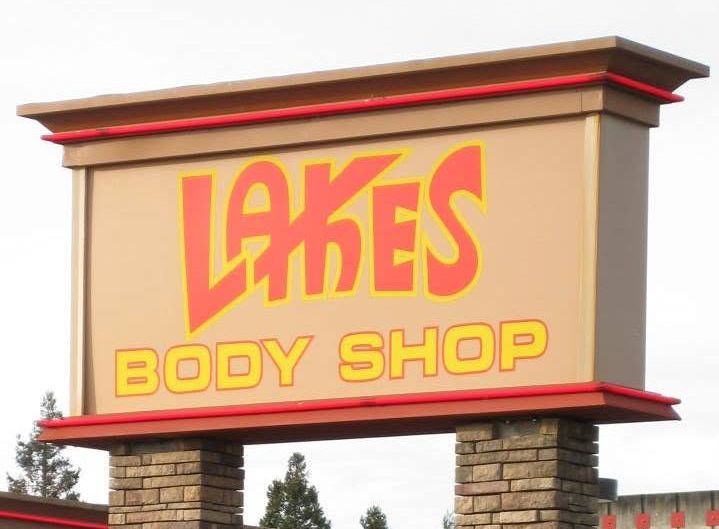 Lake&rsquo;s Body Shop sign in red and yellow on a tan roadside monument sign