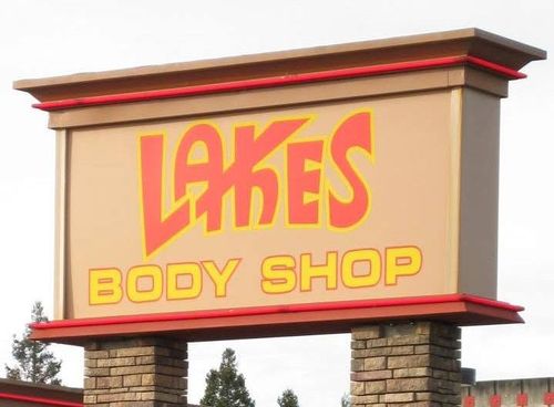 Lake&rsquo;s Body Shop sign in red and yellow on a tan roadside monument sign
