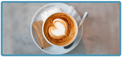 A cup of cappuccino with a heart-shaped latte art on a saucer with a spoon.