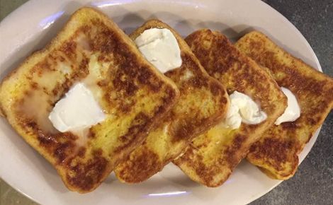 Four french toast slices with butter and syrup on a white plate.