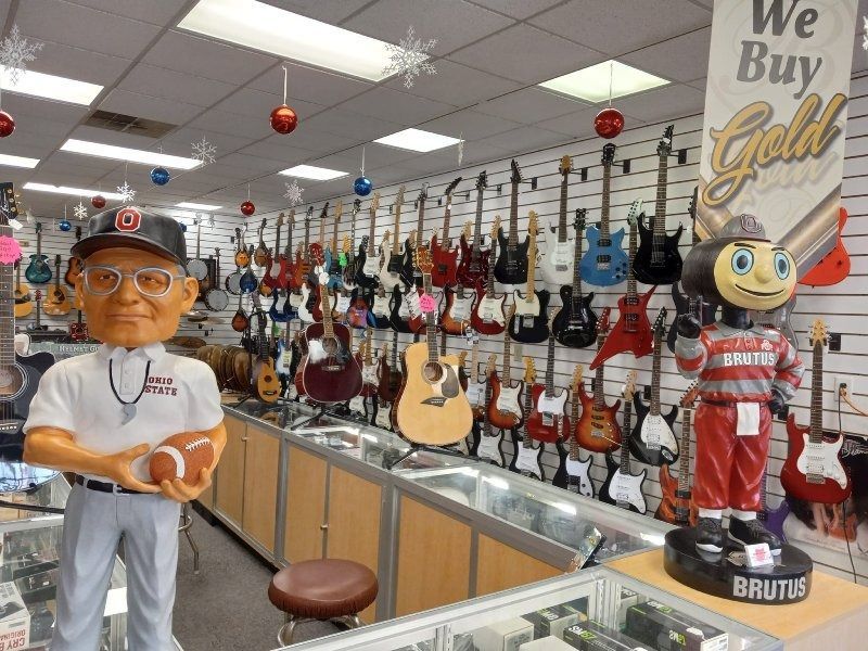 A guitar store with a mascot and a sign that says we buy gold