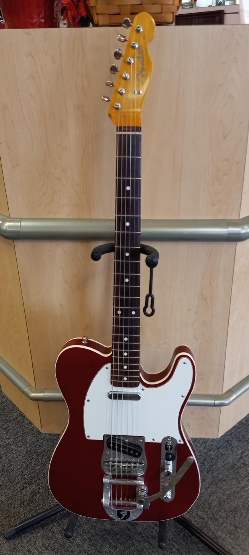 A red electric guitar is sitting on a stand.