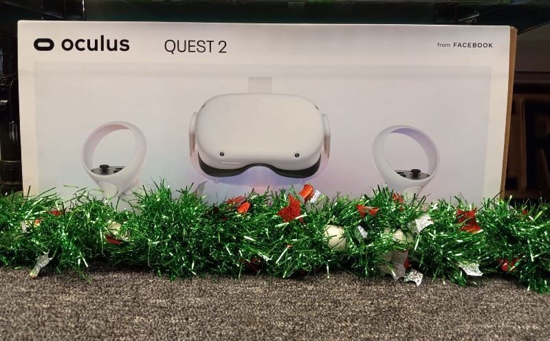 A box of oculus quest 2 is sitting on a carpet next to a christmas garland.